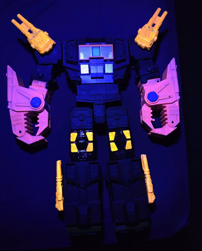 The photo shows glow-in-the-dark paint applied to a knock-off toy figure of the Transformers Decepticon Headmaster, Scorponok. The figure is bathed in black light, illuminated the pieces painted in glow-in-the-dark paint vibrantly - gun turrets, pinchers, and knee pieces.