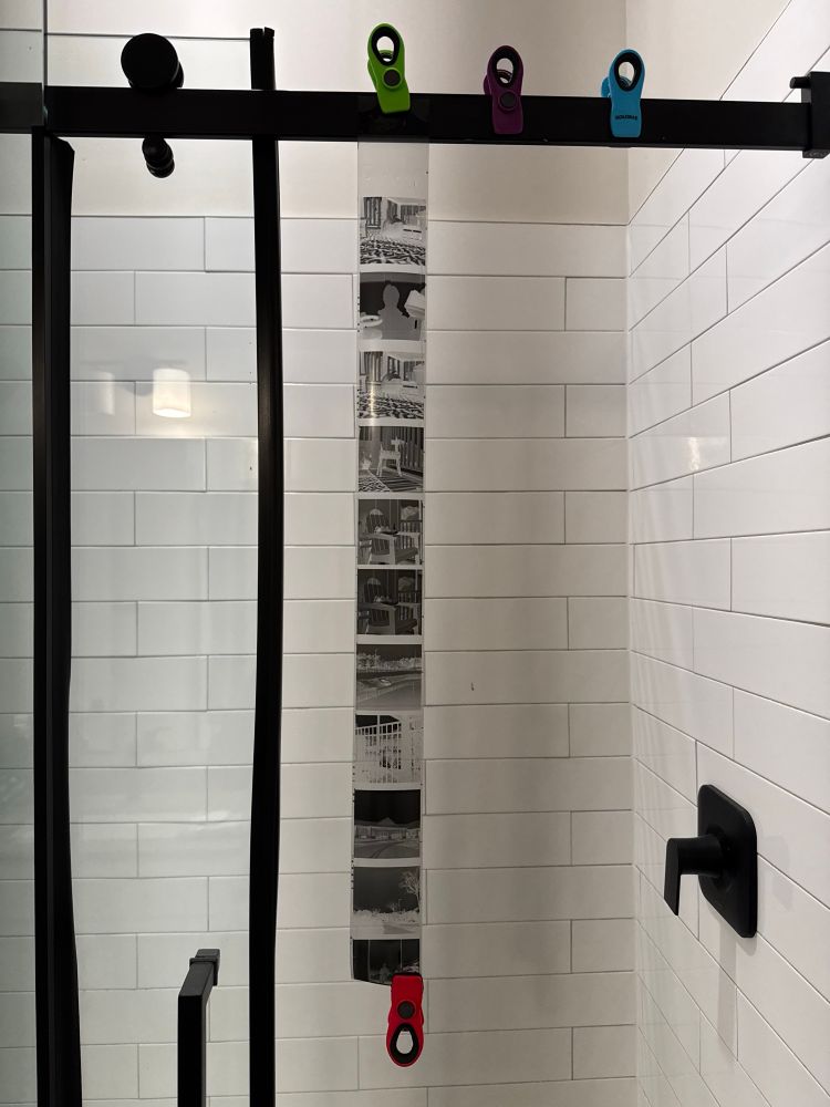 Roll of developed film is hanging to dry in a bathroom shower. 