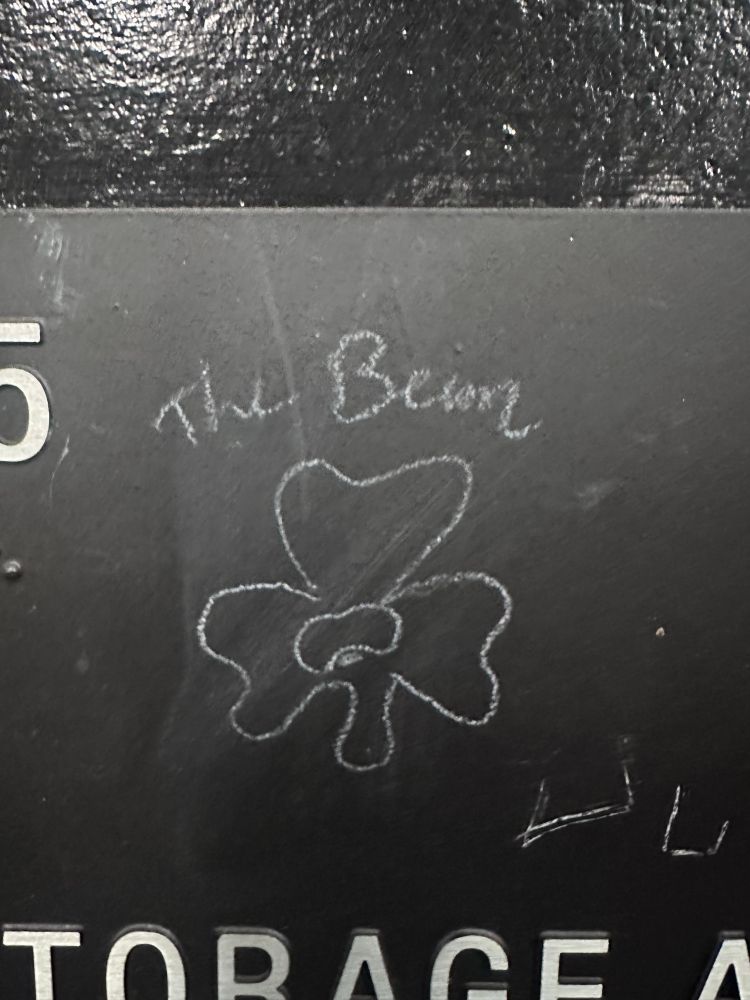 Picture of chalk graffiti on a MBTA storage and medical room door - a three leaf clover with a bean at the center and the words “the bean” over it