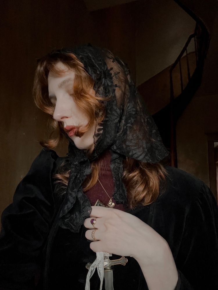 selfie taken with an iPhone. Medium length copper hair with an antique black lace veil. Wearing a black velvet jacket and a plum coloured turtleneck jumper. I’m seen holding a dagger, wearing my engaged ring close to my heart.