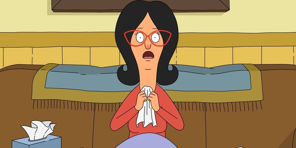 Linda belcher from Bob's Burgers - a woman sat on a sofa blowing her red nose and looking sick
