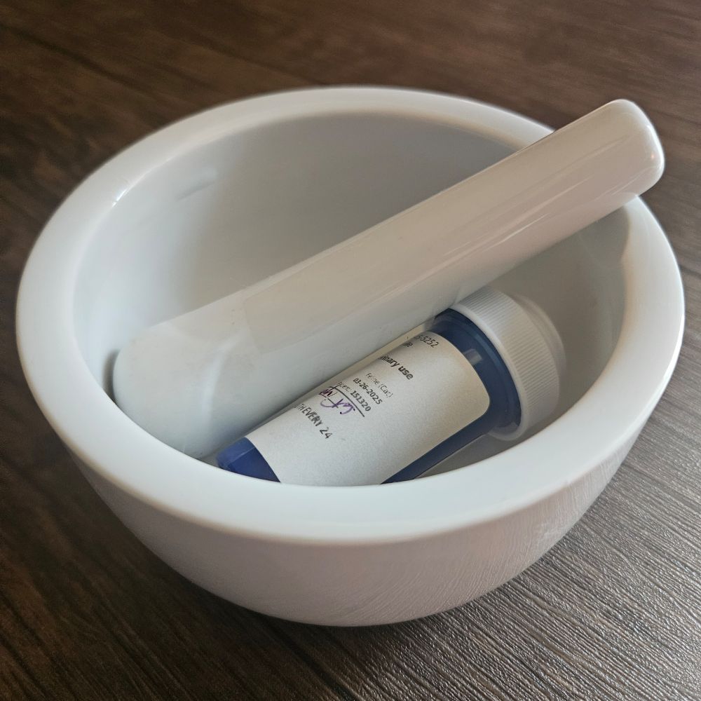 A thick, white mortal and pestle with a medicine bottle laying inside of it.