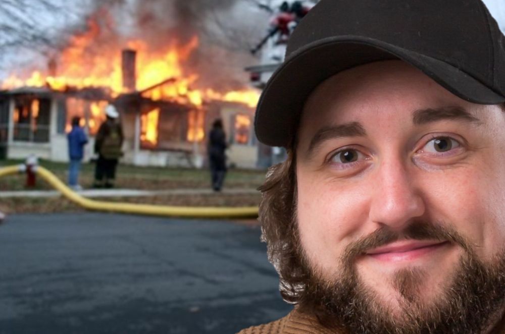 Caddicarus in a black cap, in front of a burning house.