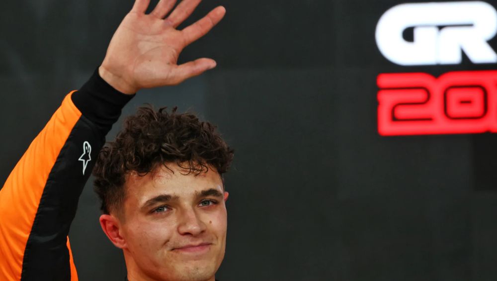 Lando Norris, barely in frame, waving at the camera.