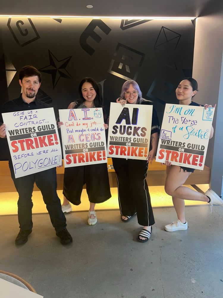 four staff from the verge holding picket signs saying things like “give us a fair contract before we’re all POLYGONE!” and “AI can’t do my job.. but maybe it could do a CEO’s”