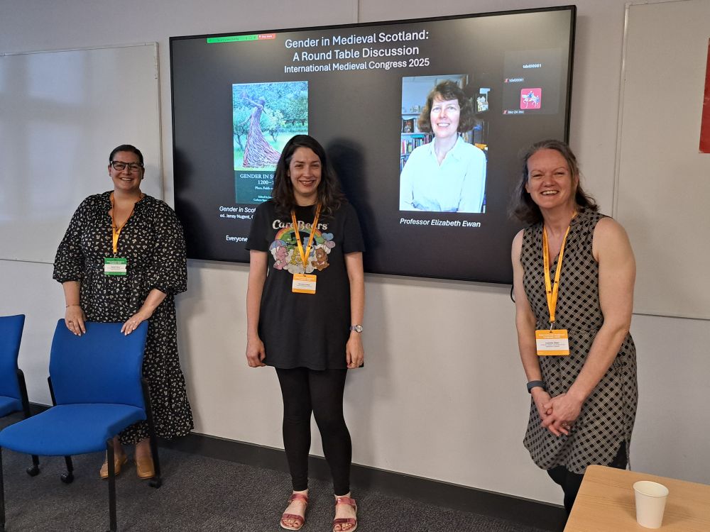 Three people looking at the camera, standing in front of a screen with presentation on it
