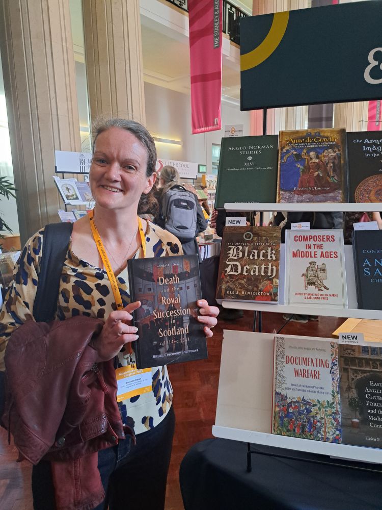 Woman holding a book, standing next to a bookstand. Book cover reads: Death and Royal Succession in Scotland
