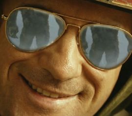 A grinning solder from Kong: Skull Island is looking at the camera, Kong's juicy ass can be seen in the reflection of his sun glasses