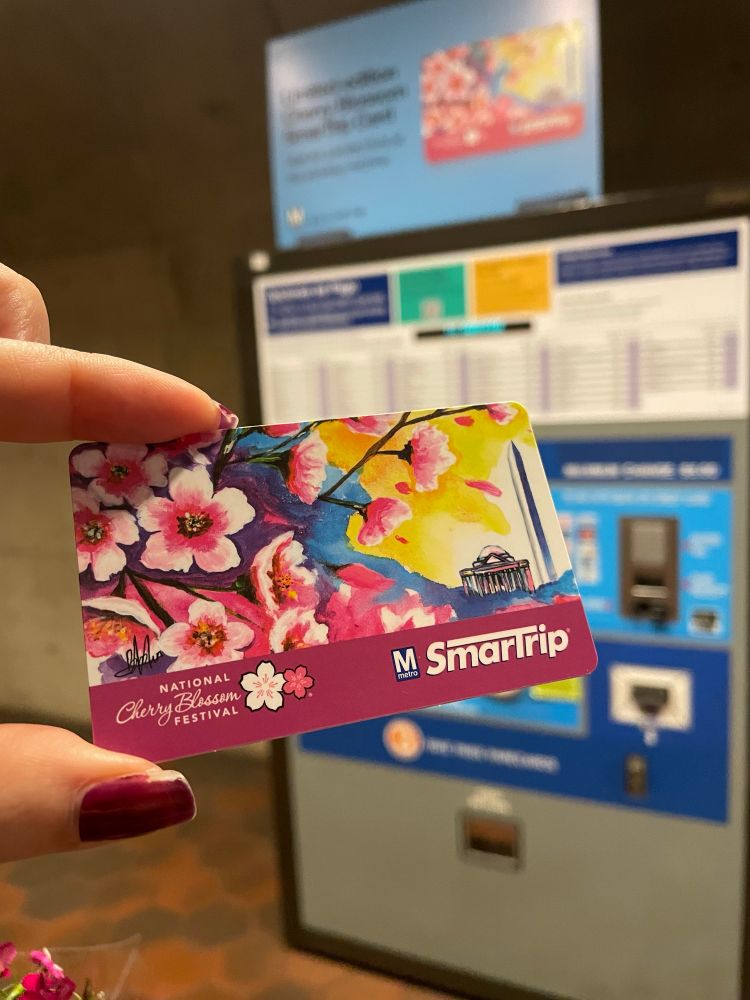 picture of the annual WMATA SmarTrip National Cherry Blossom Festival design metro card. It’s a pretty water colored theme with bright colors and big flowers, and purples, blues, and yellows in the background leading to the Jefferson memorial and the Washington monument. 