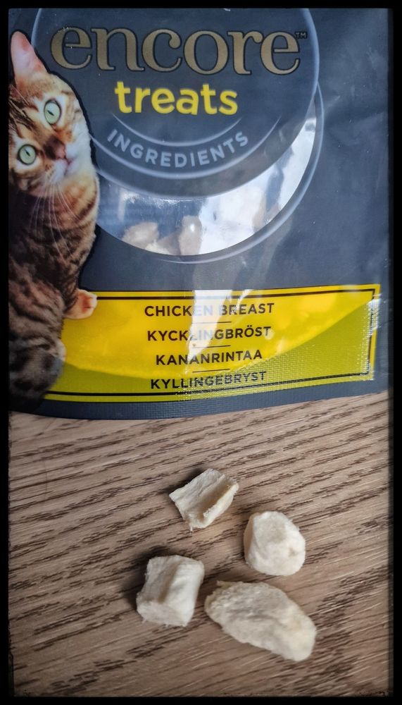 A packet of dried chicken cat treats with four little pieces on the table in front of it.