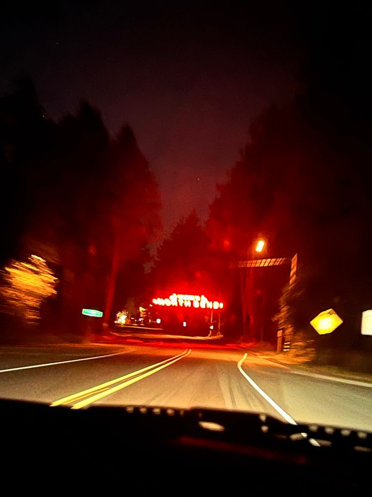 A high exposure picture from inside a car driving towards a red neon sign saying welcome to north bend 