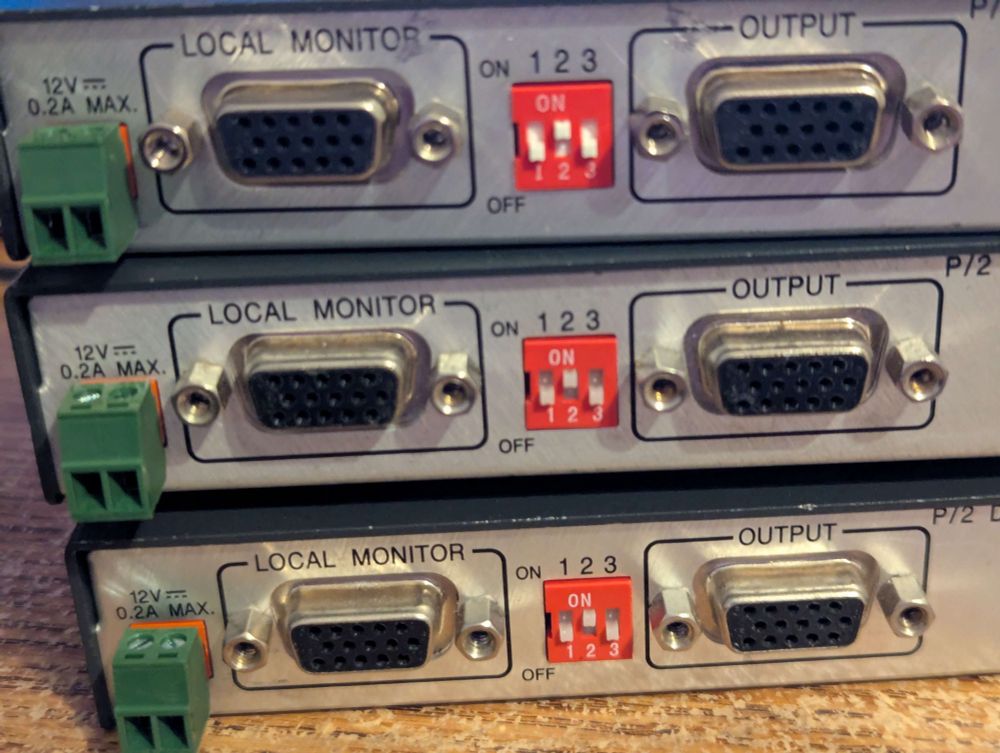 Three Extron P/2 DA2xi video amplifier/distributor boxes with 3.5mm phoenix/euroblock connector. They have two D-sub 15 (vga) connectors and a 3 dip switches. One d-sub is labeled "local monitor" and the other is labeled "output"