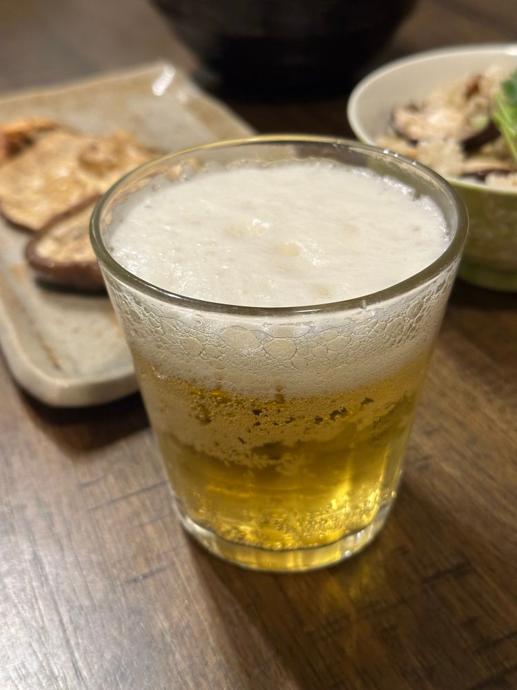グラスに入ったビールの画像。その後ろにしいたけ料理