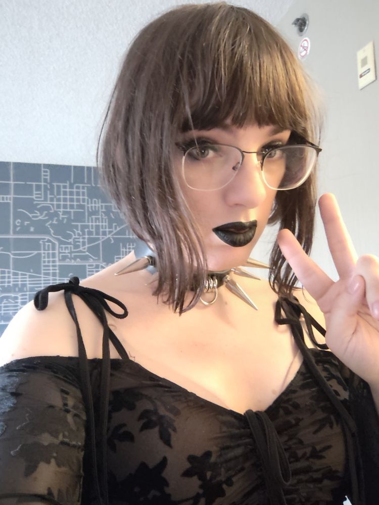 Body mirror selfie of me, a girl with short brown hair with long side tendrils. I'm wearing glasses, black lipstick, a black dress with long flowy sleeves and a choker with very long spikes