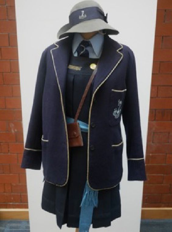 1950s blazer from Bury Grammar Schools. The blazer is dark blue with white or cream piping. There is a swan crest or logo on the breast pocket. 