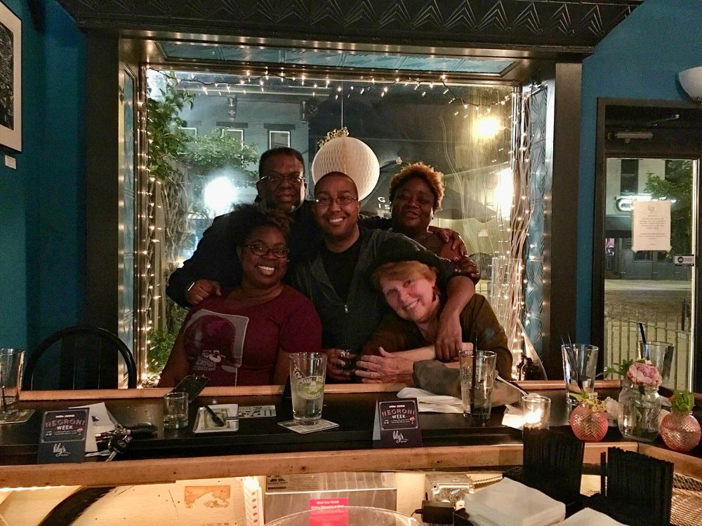 Photo of five people posing in front of a mirror in a bar
