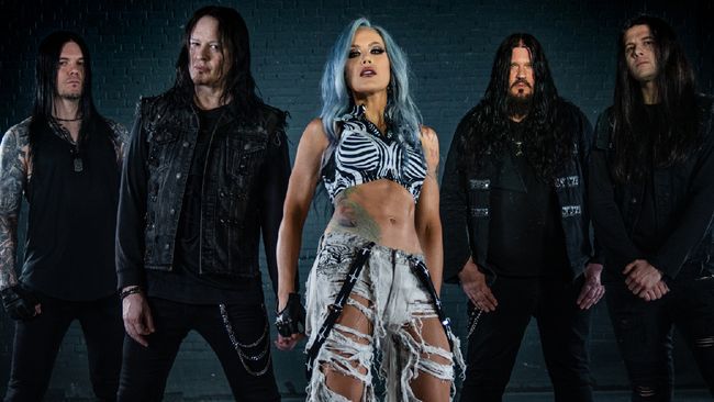 Posed shot of band "Arch Enemy". Alissa White-Gluz in the centre in shredded white pants and crop top. Left of her is Daniel Erlandsson, Michael Amott. To the right, Sharlee D'Angelo and Joey Concepcion. All the men dressed in black.  Everyone looking sterm/fierce. Publicity shot for Blood Dynasty album.