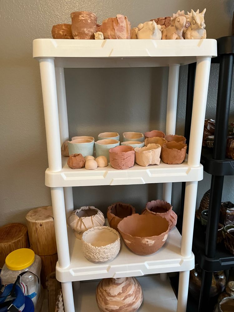 A white shelf with bisqueware pots of various shapes and sizes on it 