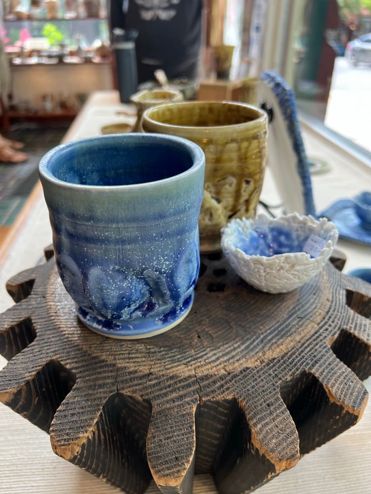 Two cups, one blue and one amber, and a small porcelain bowl sit on a riser. 