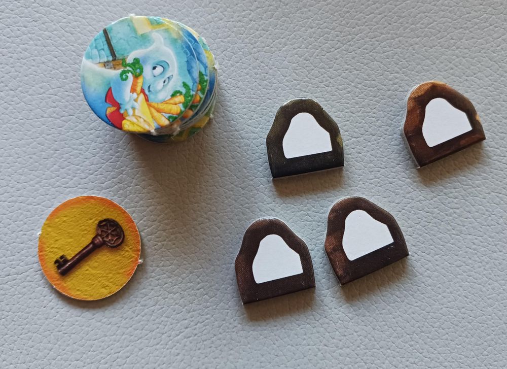 Foto der Plättchen – die runden Gespensterplättchen sind gestapelt, eines liegt mit der Rückseite nach oben daneben.

Das »Dings« sind braune Plättchen mit einem weißen geometrischen Gebilde darauf. Form und Abbildung haben eine identische Form: unten gerade, darüber in etwa – und mit sehr viel Fantasie – in Gespensterumhangform .