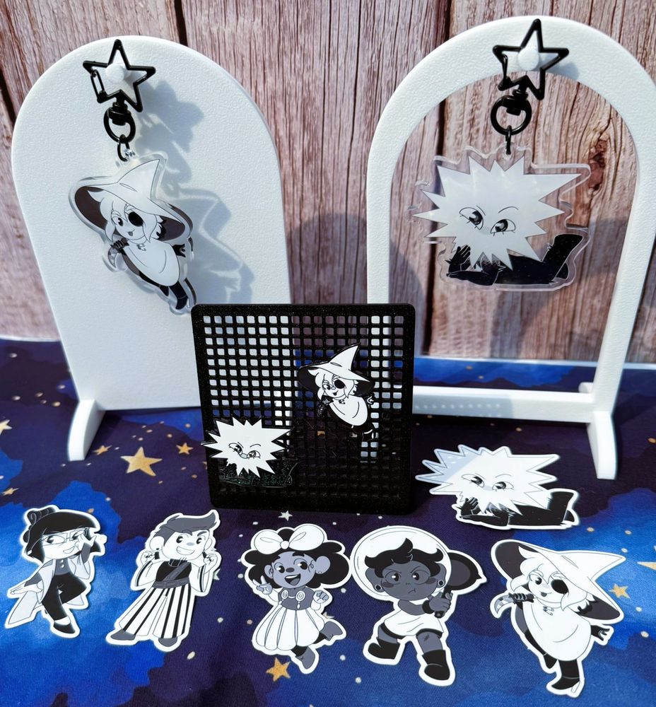 A photo of stickers, keychains, and enamel pins featuring characters from the game In Stars and Time.