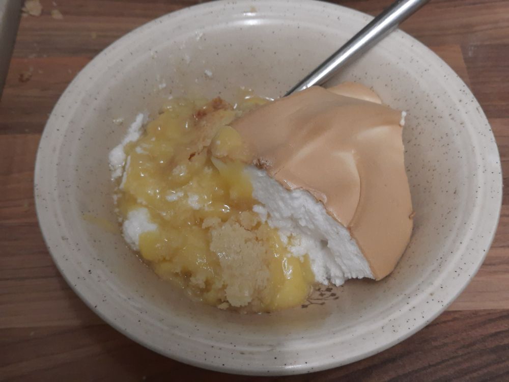 A slice of orange meringue pie in a bowl with a spoon