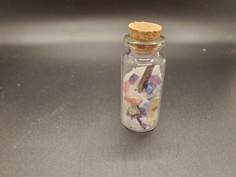 A small jar sits filled with White Sea Salt, An Iron Nail, and Amethyst, Citrine, Strawberry Quartz, and Blue Jasper stones.