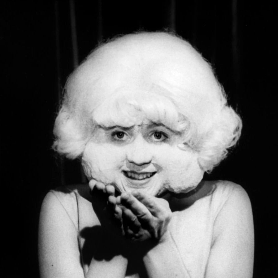the lady in the radiator from the movie eraserhead. she’s wearing weird prosthetic makeup that makes her cheeks very very puffy