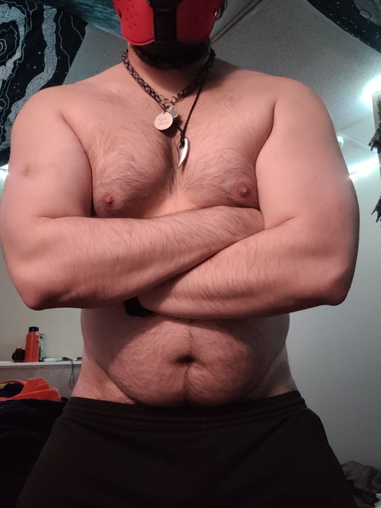 Masculine presenting person shirtless showing off from hip up. Cross arms and flexing 