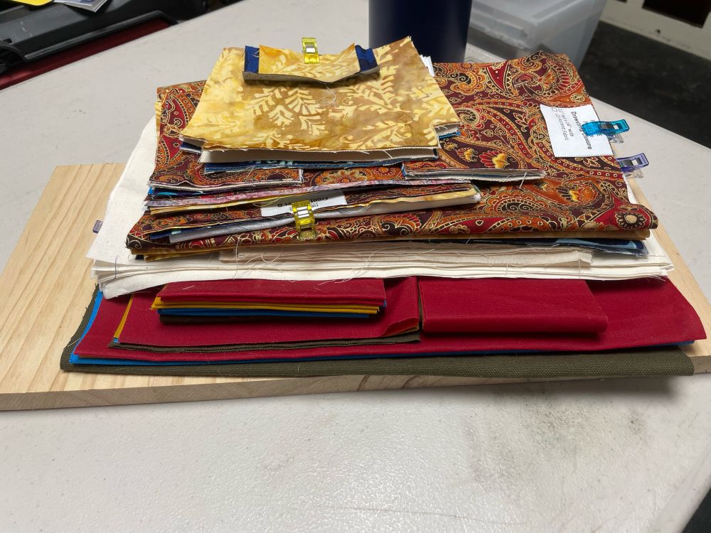 A pile of cut out tote bag and small poch parts, in assorted solid and multi-colored fabrics.
