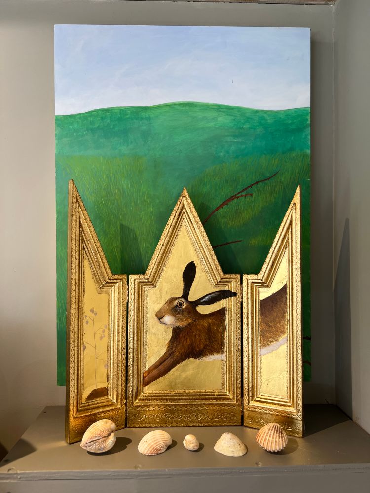 Gold Painting of a hare in front of a painting of green fields and shells 