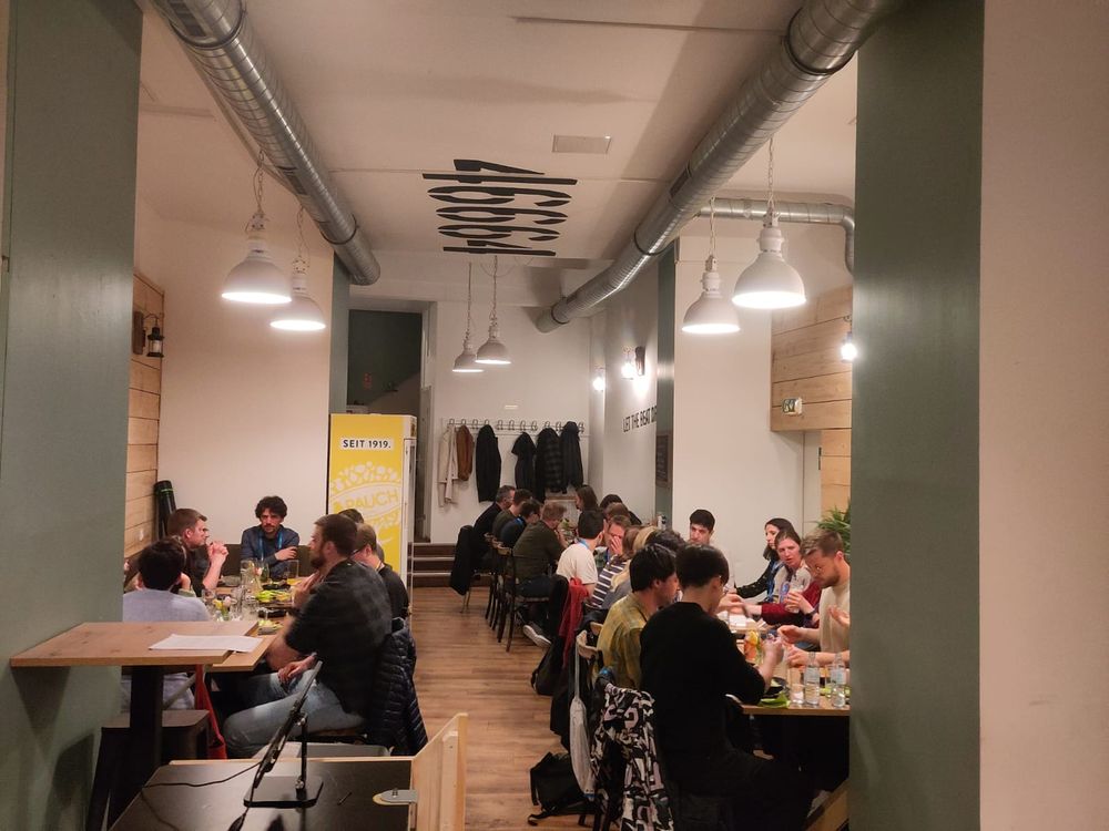 A distant view of a group of people seated around three separate dinner tables, happily enjoying their meals together.