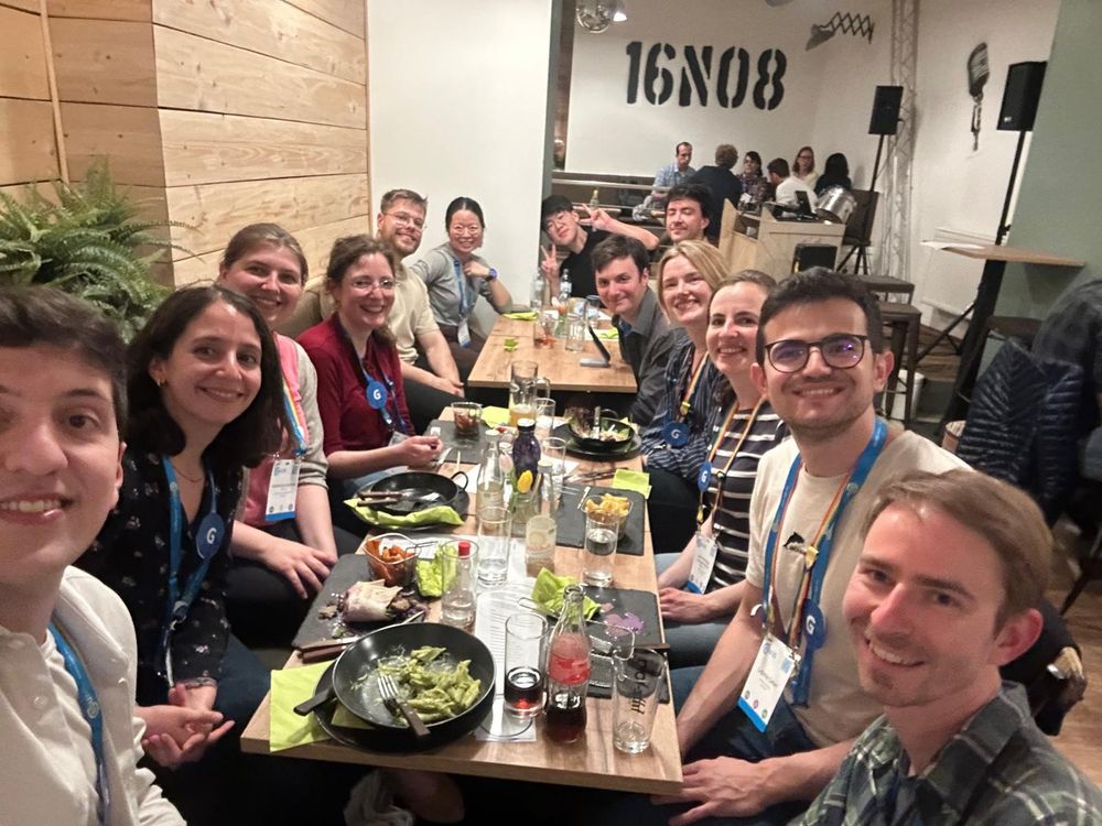 A group of people sitting around a dinner table, all smiling and looking at the camera, with a warm and joyful atmosphere.