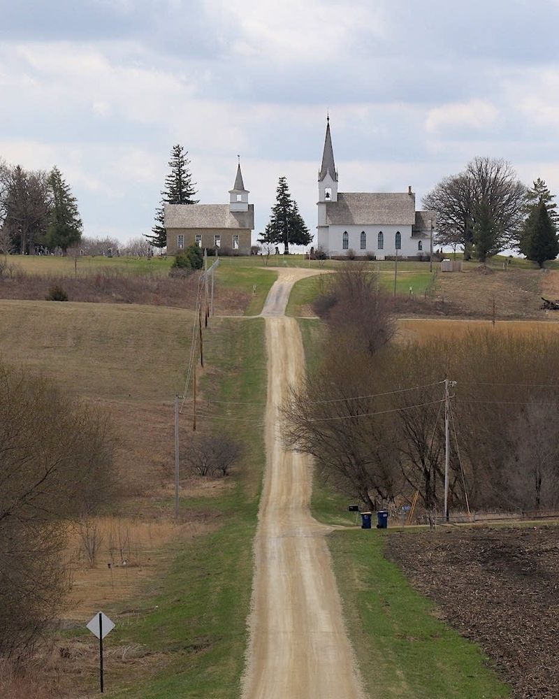 Two church buildings atop a hill at the end of a gravel road.