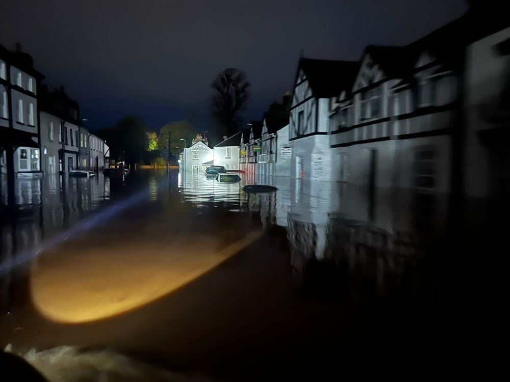 Very flooded street at night: the very top of a few parked cars are visible.
