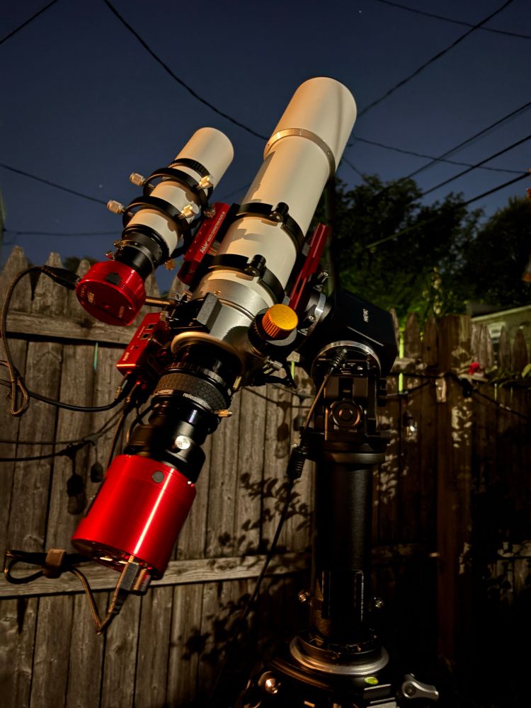 a small white telescope with a smaller white telescope on top of it, all in front of a wooden fence
