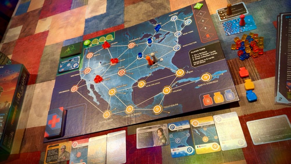 My kitchen table with the Pandemic Hot Zone: North America Game set up. The game board shows the continent of North America with major cities as the spaces and little cubes on some cities indicating level of infection. 