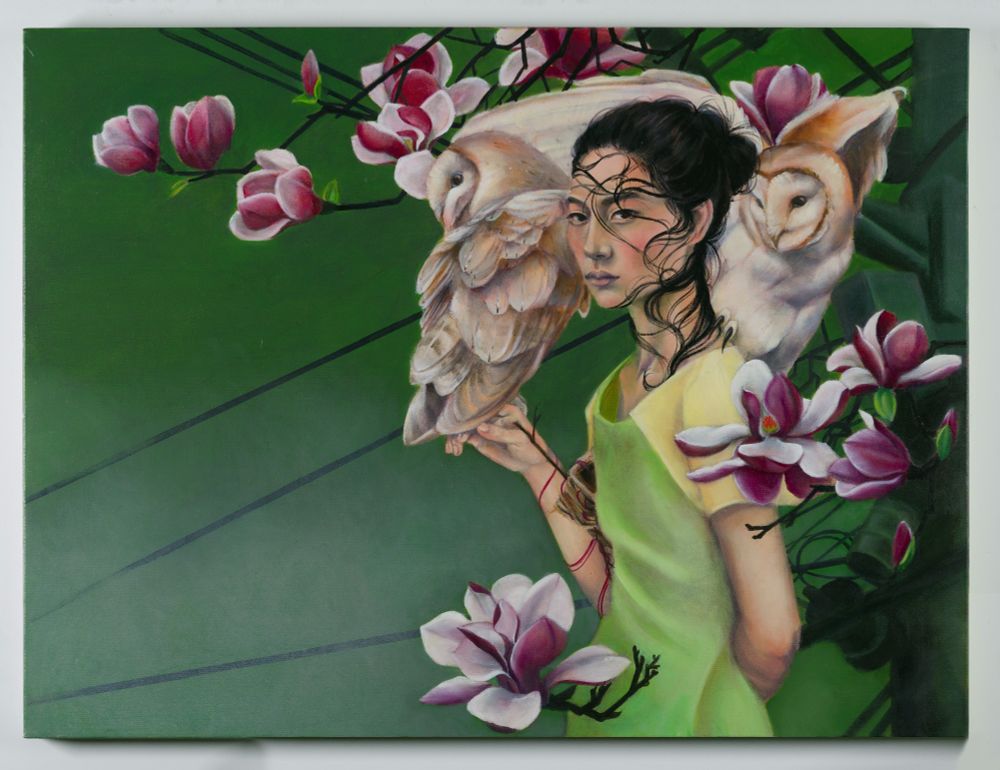 Woman with 2 barn owls perched on her surrounded by magnolia flowers and powerline mast behind them.
