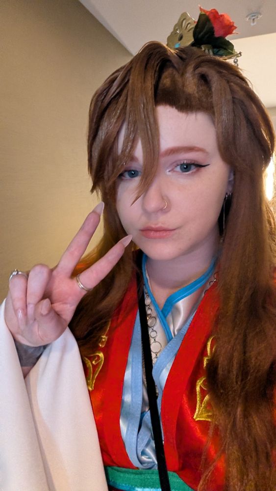 Picture of me in my Li Yu cosplay. Red outer robe with light blue and cream inner robes, styled brown wig, and gold crown and red flower in the hair 
I'm holding up a peace sign for the pose