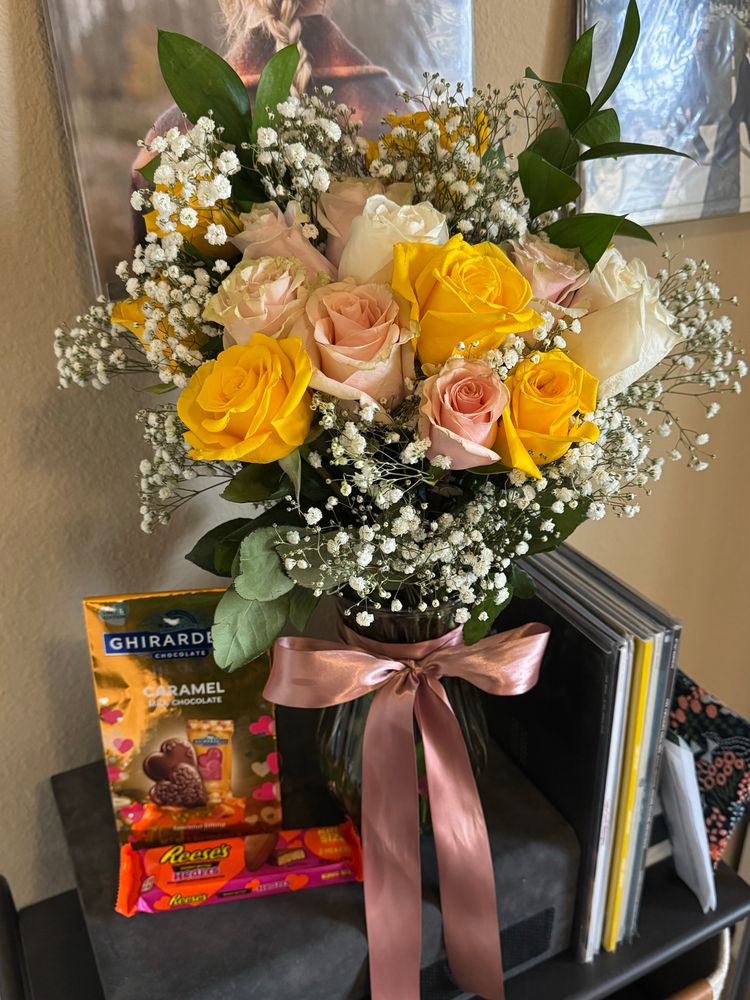 a vase of pink, yellow, and white roses next to a bag of caramel chocolate hearts and a packet of reese’s hearts 