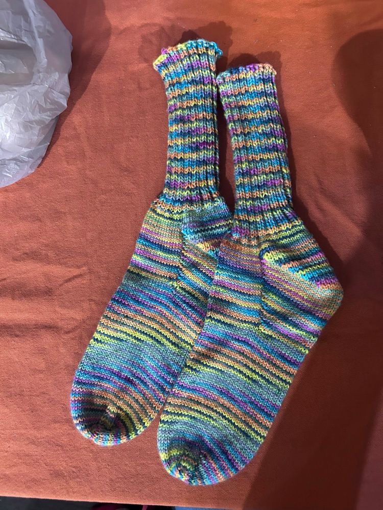 Rainbow socks on an orange background. Socks are a vanilla main with a 2x2 ribbed cuff.