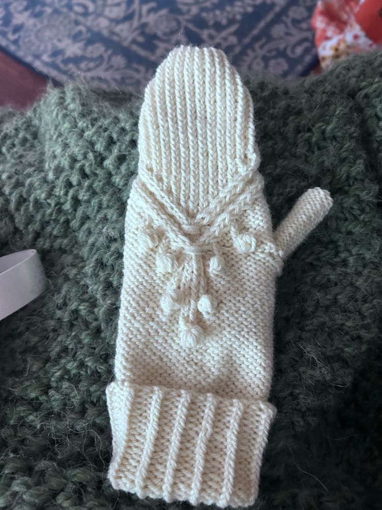 A textured mitten in cream on a dark green background knit blanket. 
