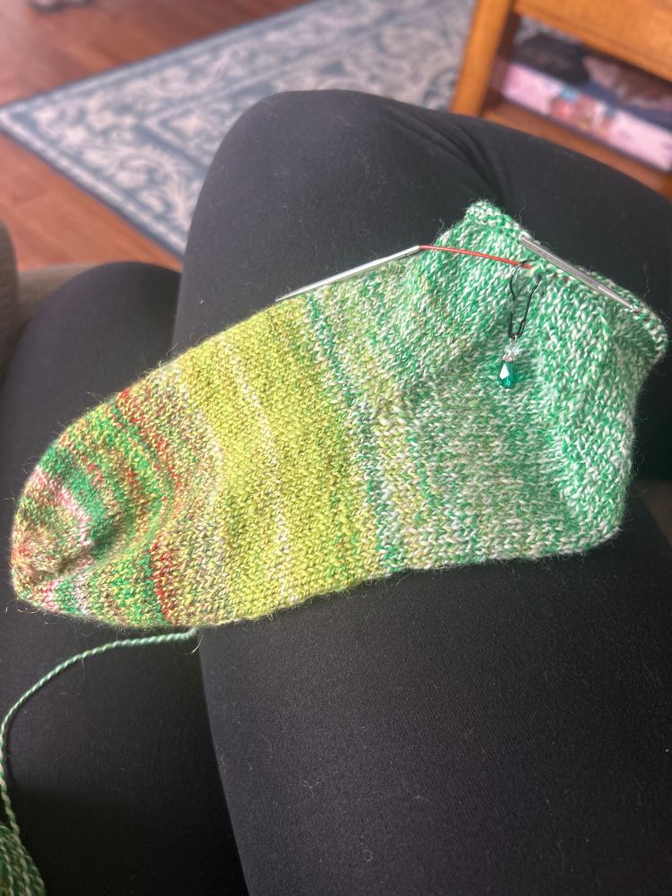 A handspun, Christmas colored sock, minus the ribbing, on a black background. 