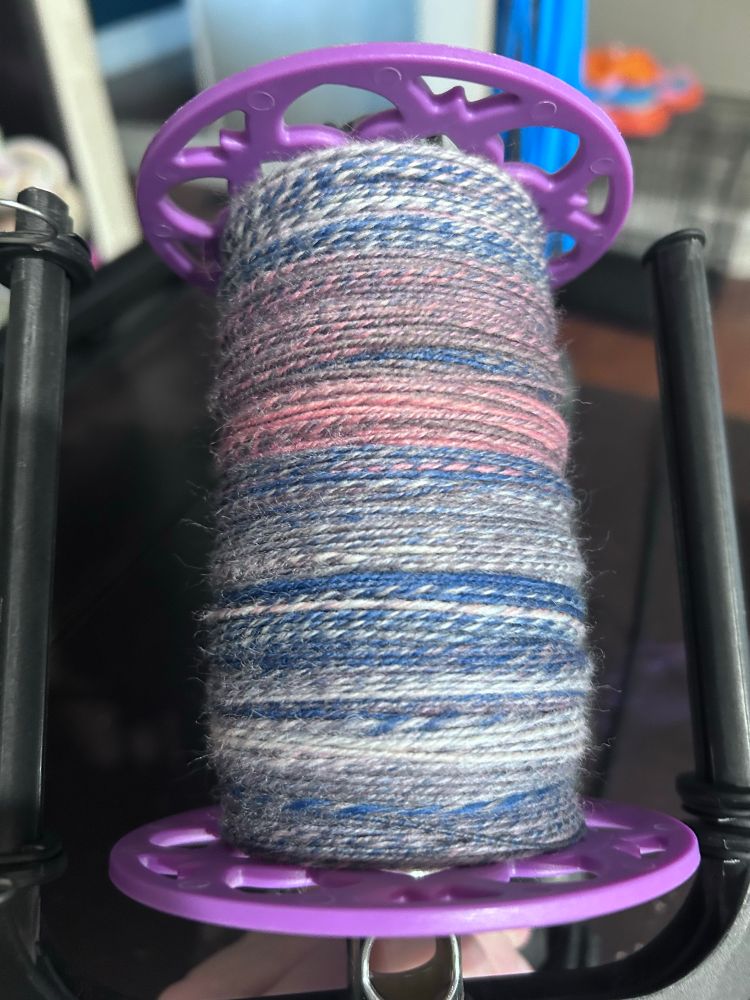 Multicolored handspun yarn, chain plied on a purple bobbin. 