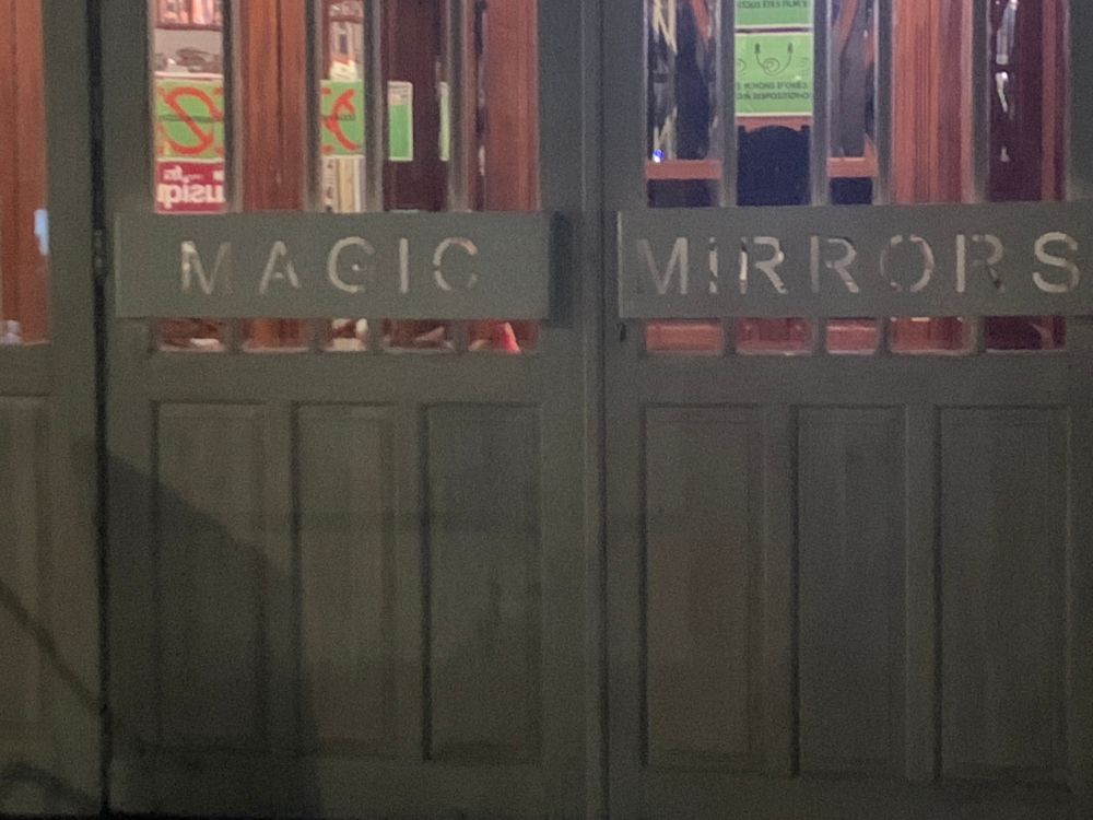 L’entrée du Magic Mirrors (un chapiteau très cosy) : deux portes grises, vitrées. L’une porte ce mot ‘‘MAGIC’’ et l’autre ‘‘MIRRORS’’  en lettres réfléchissantes.