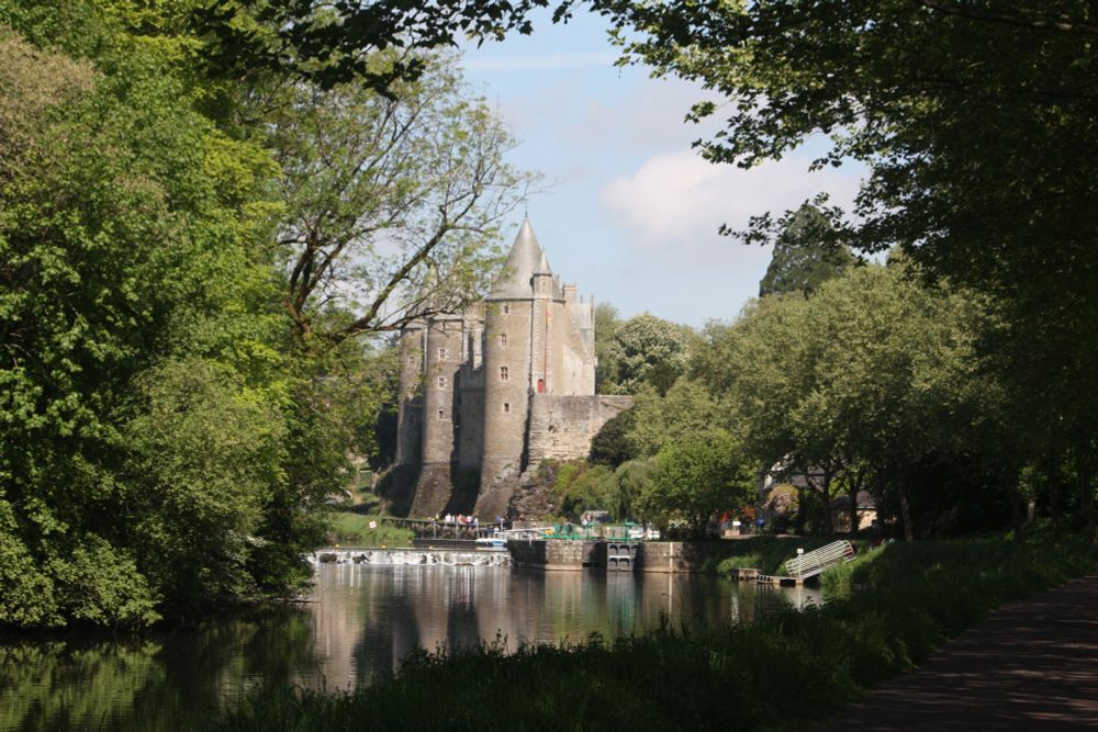 Le château de Josselin au bord de l’Oust canalisé (ou voit une écluse) Beaucoup d’arbres et les trois grosses tours en pierres ocres surmontées d’un toit en ardoises grises