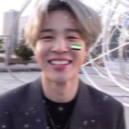 Jimin smiling with blonde hair, an Aro pride flag on his cheek and sparkles