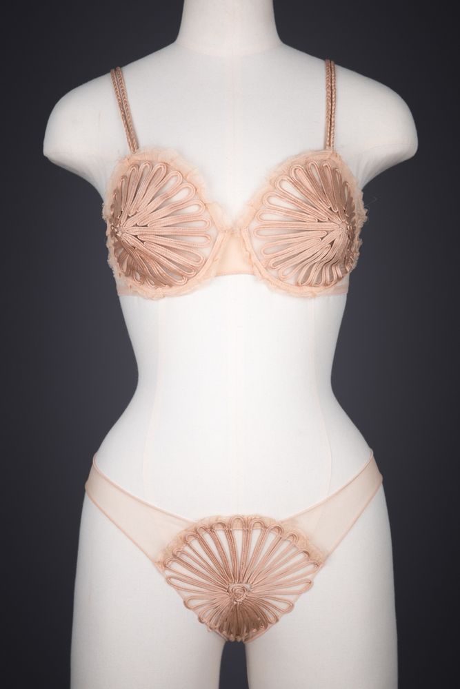 A bra and brief set with extensive ‘soutache’ silk braid embroidery. The bra has a dramatically pointed bustline and uses a combination of underwires and boned structures throughout the cup to achieve a silhouette reminiscent of 1950s foundationwear. The soutache embellishment covers the body of the cups, with small flourishes of the technique on the bra wings. Plaited silk braid forms the shoulder straps, and the interior bone and wire channels are encased in silk. Raw edged silk georgette trims the bra neckline.

The main body of the knickers is formed of a sheer synthetic stretch mesh, finished with an extremely narrow babylock stitched edge. The centre panel of the briefs is embellished with further soutache embroidery, with raw cut silk georgette trimming the waist edge.

These garments are from the ‘Feuillage’ range (which translates as ‘foliage’) of the Créateur collection, a collaboration between French couturier Jean Paul Gaultier and heritage luxury lingerie house La Perla. 