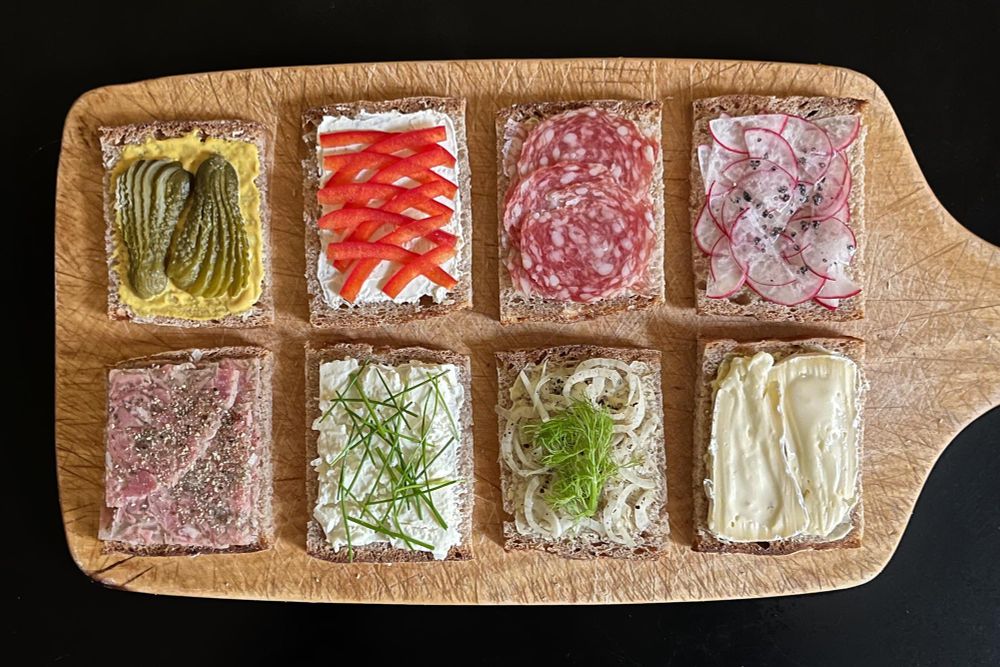 Auf einem Holzbrett acht einander paarweise zugeordnete Brotscheiben, Belag: 
– Butter, Senf, Gewürzgurken / Kräutersülze, Pfeffer
– Frischkäse, Paprikastreifen / Schafskäse, Schnittlauch
– Butter, Salami /  Fenchel, Fenchelsamen, Pfeffer, Vulkansalz, Fenchelgrün
– Butter, Radieschen, Vulkansalz / Camembert