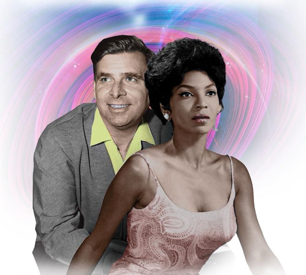 Gene Roddenberry smiles expressing joy and wistfulness in a gray suit jacket and yellow dress-shirt sitting behind Nichelle Nichols who expresses wistfulness and determination in a pale pink paisley strappy top.